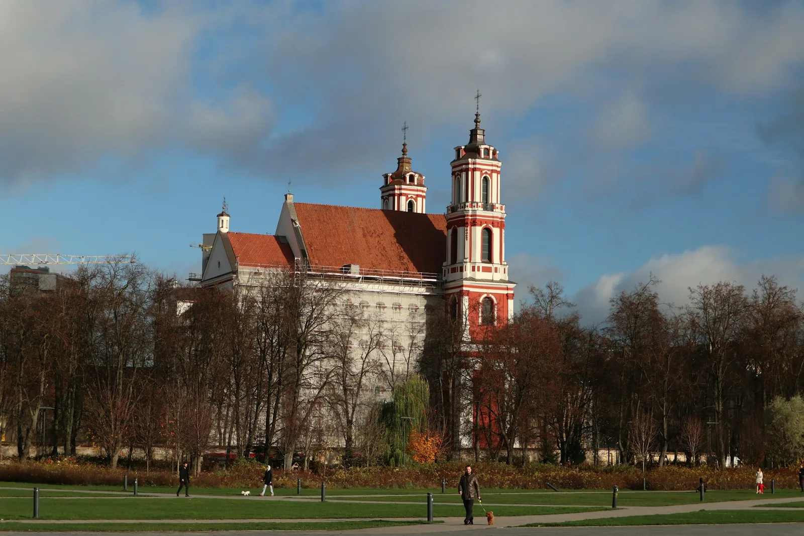 The red-and-white Baroque twin towers of a historic Vilnius church rising above autumn trees in a city park